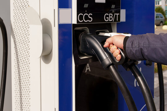 Man hand holding black CCS charging plug at public station. Interaction with infrastructure during electric car charging