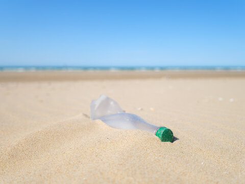 Environmental waste problem on the sea coast. Plastic bottle on the beach. Plastic trash buried in the sand.
