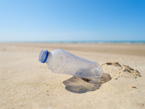 Environmental waste problem on the sea coast. Plastic bottle on the beach. Plastic trash buried in the sand.