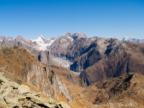 Panoramic aerial view of glacier surrounded by mountain peaks in Switzerland. Alpine glacier landscape with snow and rocks on sunny day.