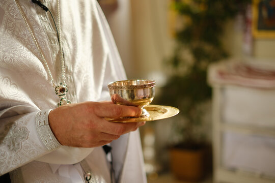 Priest holding a golden communion chalice during orthodox christian baptism ceremony in church.