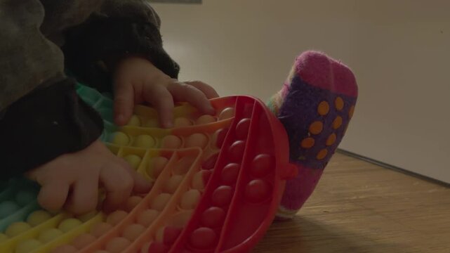 Child practicing finger coordination and fine motor skills by pressing individual bubbles on a sensory pop it toy.