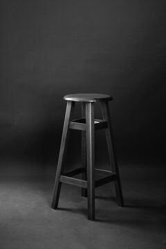 Black wooden bar stool standing in dark studio on black background.