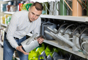 Young man shopper choosing watering pot in gardening department of hardware store © JackF
