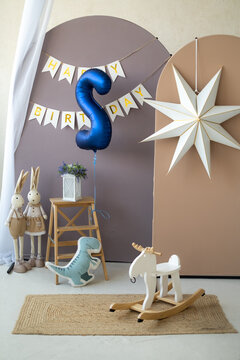 Birthday photo zone setup with number five balloon, bunting banner, paper star, and rocking moose toy in nursery studio.