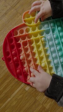 Child&rsquo;s fingers pressing soft silicone bubbles on a colorful pop it toy during tactile sensory play.