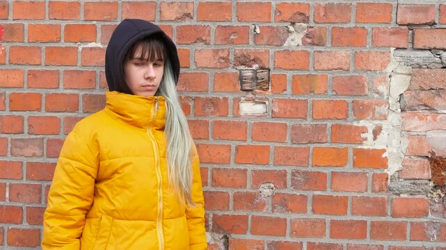 Stressed teen on background of a brick wall. A view of stressed young girl with trouble stand by the brick building during day time