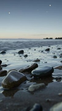 Vertical video: Lapping shallow wave moving over smooth wet pebbles at shore, glinting as tide ebbs