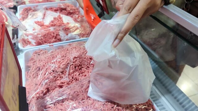 An unrecognisable woman uses a scoop to transfer fresh ground beef into a plastic bag, carefully packaging the meat for purchase at a market or supermarket