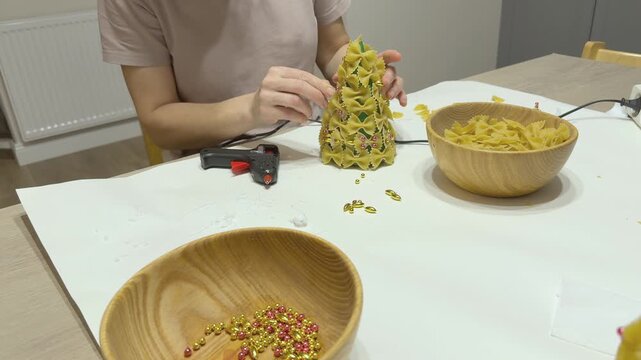 Pasta Christmas tree craft in progress with small decorations added by hand. Creative holiday activity for children and adults. Useful for DIY channels, seasonal blogs, school projects and festive