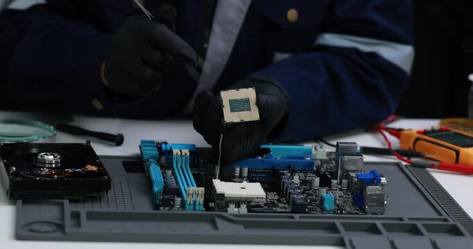 Technician in protective gloves repairs a computer motherboard with a screwdriver at a workbench, electronics maintenance and hardware troubleshooting.