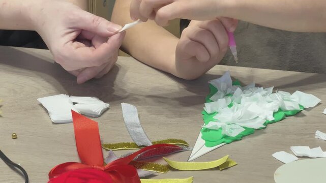 Close view of child hands shaping plasticine and attaching tissue paper to Christmas tree craft. School or kindergarten holiday activity. Great for educational visuals, kids creativity and seasonal