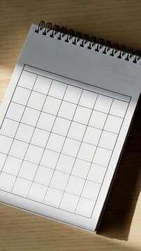 Vertical video: Curling page turning on spiral notepad over wood desk, revealing grid