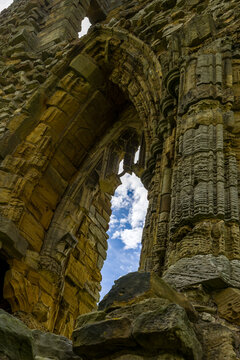 Ruined Gothic abbey arch seen from low angle looking up, detailed eroded stonework and crumbling window tracery, ancient monastic heritage site