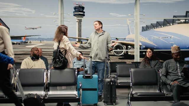 Upset woman in airport scolding man after bumping trolley into her while hurrying to catch plane; angry tourist yelling at traveler for bashing her luggage in busy departure terminal.