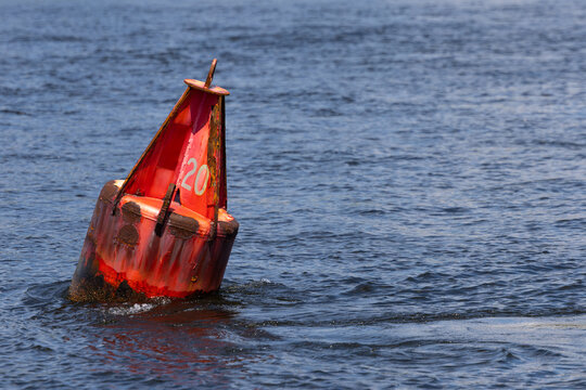 Red Nun Buoy Number 20 Floating in Choppy Blue Water &mdash; Weathered Navigation Channel Marker With Peeling Paint and Rust