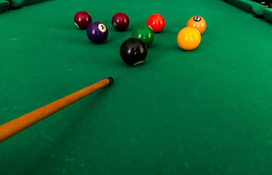 Colorful and numbered billiard balls on a green felt pool table with a wooden cue stick in a gaming environment