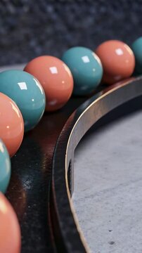 Vertical video: Rolling turquoise-coral beads along metal groove in studio on camera pan, for demo