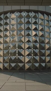 Vertical video: Start panning camera filming curved metal wall at plaza, showing shifting light