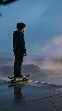 Vertical video: Balancing teen on skateboard spotting wet ramp, shifting weight at skatepark