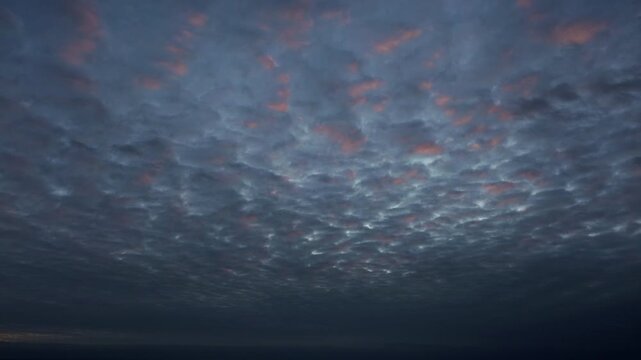 Altocumulus clouds over dark sea at colorful sunrise in Gulf of Mexico as drone pov moves forward showing red purple sky gradient and glowing sky texture over calm ocean water in Ciudad Madero