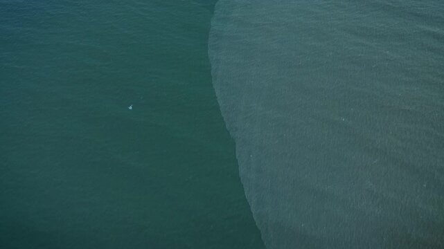 Top down view of freshwater and saltwater meeting at Panuco River mouth creating natural water color divide at Miramar Beach breakwater in Gulf of Mexico Ciudad Madero Tamaulipas during drone pov