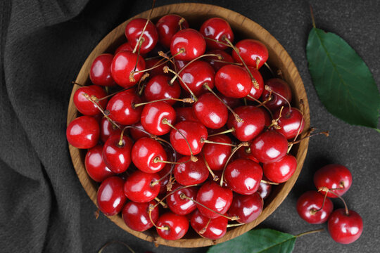 Fresh ripe red sweet cherries in wooden bowl on dark textured stone background with green leaves and black linen towel. Summer fruit, berry, harvest, healthy organic food
