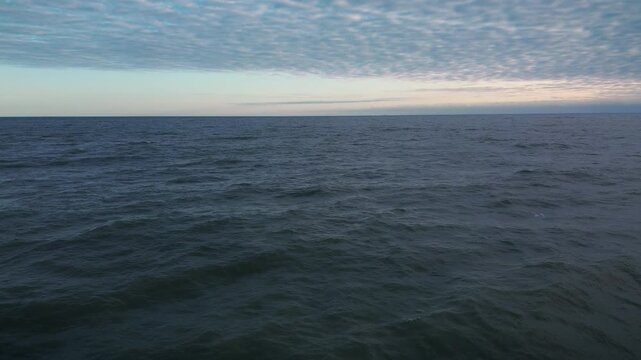 Altocumulus clouds over dark sea at colorful sunrise in Gulf of Mexico as drone pov moves forward showing red purple sky gradient and glowing sky texture over calm ocean water in Ciudad Madero