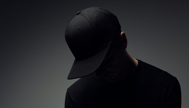 High-angle three-quarter view blank black baseball cap snapback mockup on man looking down against dark studio background
