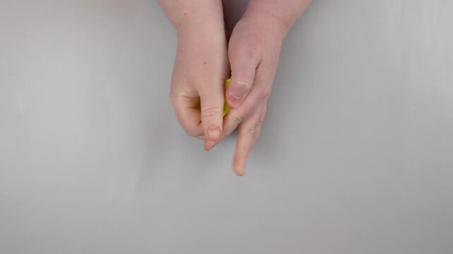 Children's hands begin to crumple a smooth sheet of bright yellow paper on a neutral background. The initial stage of creasing, the moment of transition from neatness to creative chaos.