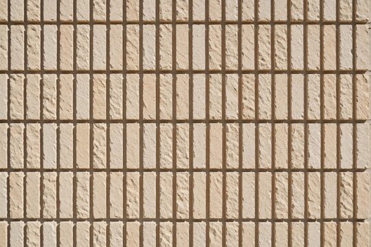 Beige clinker brick wall with vertical pattern. Textured stone surface shows rectangular blocks in neat rows. Building facade material provides neutral background for architecture design construction
