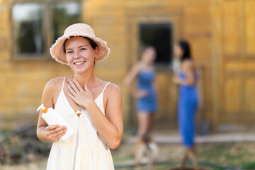 Obraz premium Before working at garden bed, girl farmer protects skin with sunscreen. Sunburn prevention, skin protection and prevention of skin diseases. Country house in background