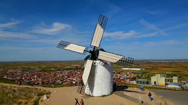 White windmill with a view of the cityscape and a blue sky in the background, aerial view, Consuegra, Toledo, Castilla-La Mancha, Spain