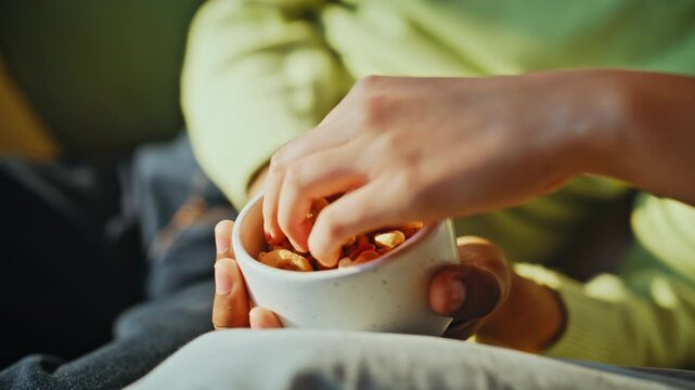Mixed nuts bowl closeup hands sharing snack. Healthy vegan snacking home sofa.