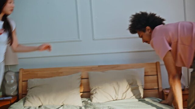 Man jumping bed laughing girlfriend. Multiracial pair fooling around bedroom.