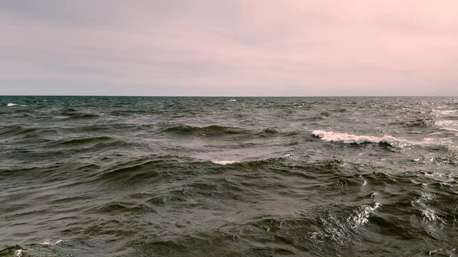 Scenic view of choppy Great Lakes water and whitecaps glowing beneath a subtle pink sky. Captures tranquil nature, beautiful water textures, and open horizon scenery in Michigan.