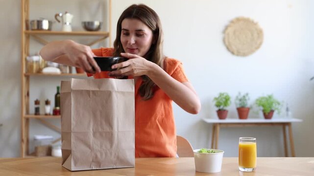 Food delivery. Woman taking container with meal out of paper bag at table indoors