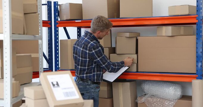 Worker with clipboard checking boxes on shelves in warehouse