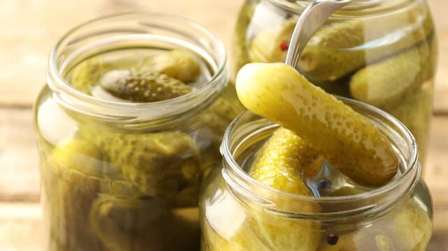 Taking pickled cucumber from glass jar at table, closeup