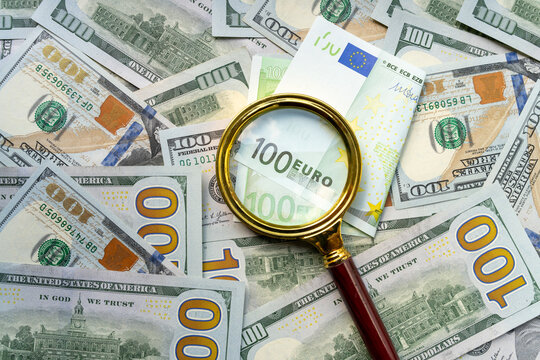 Magnifying glass enlarges 100 euro banknote against collage of 100 US dollar bills, highlighting currency exchange, euro-dollar rivalry, and financial market competition. Real Photo
