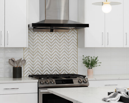 A white kitchen detail with a stainless steel range hood over a gas range, a gold and marble chevron backsplash, subway tiles, and a marble countertop.