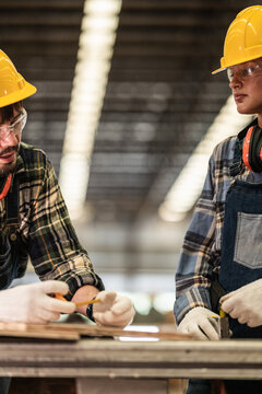 Bearded carpenter in safety glasses and his female partner check a tape measure reading in a close two shot during a research study on AGI driven robotics and transport in the wood industry