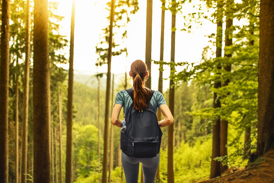 Female hiker with backpack exploring a beautiful sunlit forest during an outdoor nature adventure