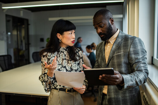 Coworkers comparing a paper report with a tablet in an office