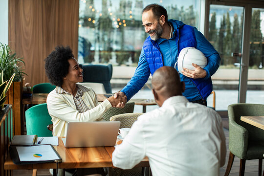 Contractor greeting clients with handshake in cafe