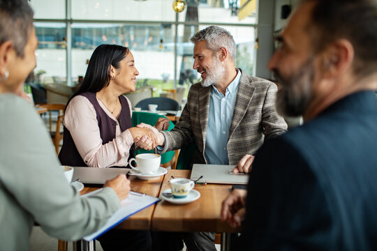 Two professionals shaking hands at a cafe meeting