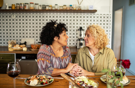 Two women holding hands over dinner at home