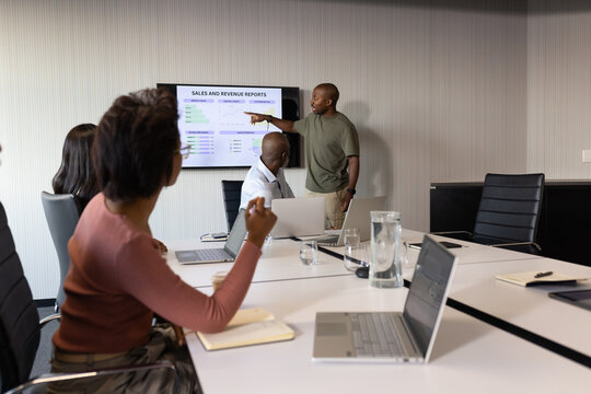 Diverse coworkers in office attire watching presenter pointing at screen with laptops, copy space