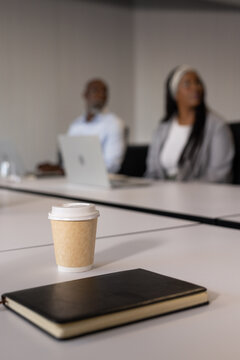 African American coworkers in office wear discussing at meeting table with coffee cup and notebook