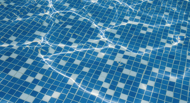Abstract shimmering sunlight on blue and white mosaic tiles underwater in a swimming pool